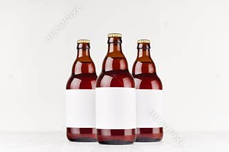 Three brown belgian steinie beer bottles 500ml with blank white label on white wooden board, mock up.