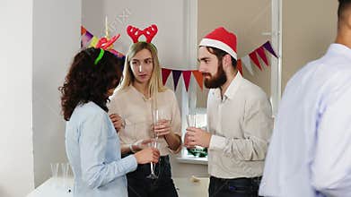 Young office workers talking and holding glasses with sparkling wine during christmas party in the office while their