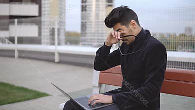 Attractive businessman in black suit using laptop sitting outdoor