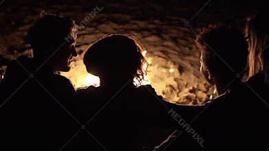 Back view of diverse group of people sitting together by the fire late at night and embracing each other. Cheerful