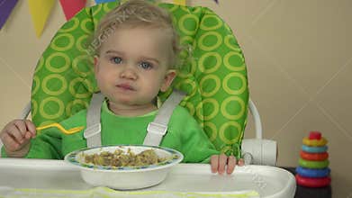 Little girl practice eat gruel with spoon sit on baby chair. 4K