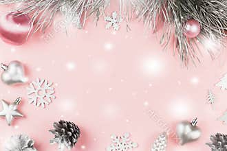 Christmas frame with fir branches, conifer cones, christmas balls and silver ornaments on pastel pink background