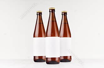 Three brown NRW beer bottles 500ml with blank white label on white wooden board, mock up.