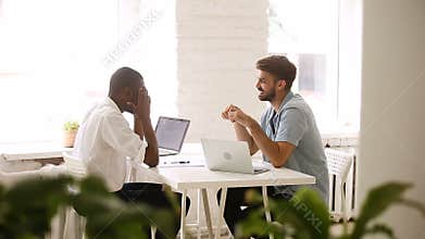 African american and caucasian young businessmen talking laughing at workplace