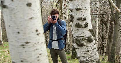 Man in woods looking and shoot photos in camera.Following side.Real people Millennial traveller backpacker adult male