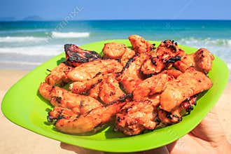Cooked Chicken Wings on Green Plate against Azure Sea on Beach