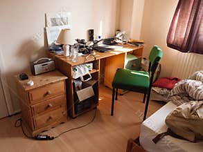 Soft light lit student bedroom desk and chair clutter messy