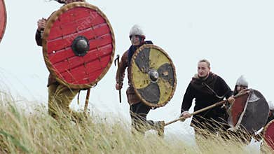 Group of Viking with shields running forward on the meadow and raises sword