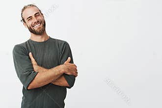 Attractive swedish man with stylish hair and beard laughs at funny story from friend with crossed hands and closed eyes.
