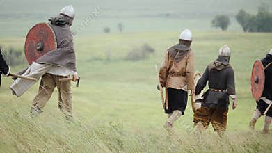 Group of Viking with shields walking forward on the meadow