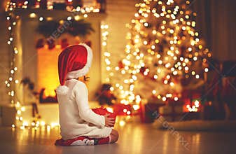Child girl sitting back in front of Christmas tree on Christm
