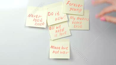 Closeup woman`s hands stick yellow sticker paper sheets with motivation phrases on a white board.