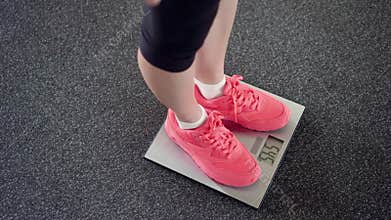 Girl measuring her weight on electronic scales. Slim female legs in pink sneakers on digital balance