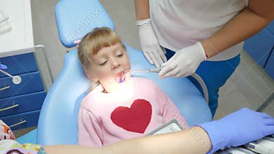 Child with open-mouthed lies on dental armchair at treatment by doctor with instruments in hands in clinic