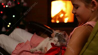 Young girl holding her christmas present by the fire - caressing a kitten