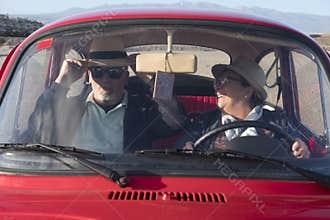 Seniors couple driving and having fun inside an old red car