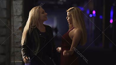 Two female friends having fun at party, moving to music on dance floor, laughing
