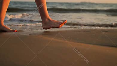 Female feet walking barefoot on sea shore.