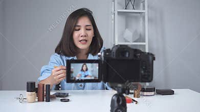 Happy smiling asian woman or beauty blogger with brush and camera recording video and waving hand at home.