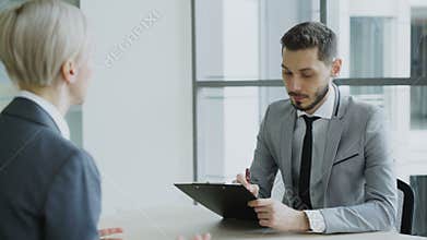 HR male manager having job interview with young woman in suit and watching her resume application in modern office