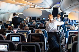 Interior of large commercial airplane with stewardesses serving passengers on seats during flight.
