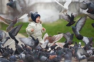 Street portrait of the little boy feeding pigeons with bread