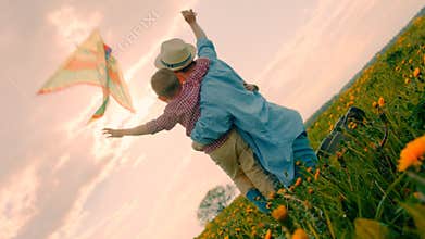 Mother and her little children are looking at flying kite at sunset light at field