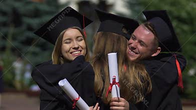 Friends graduates in academic dresses congratulating and hugging each other