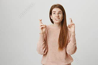 Concept of human expressions and body language. Adorable ginger girl standing with crossed fingers, biting lip and