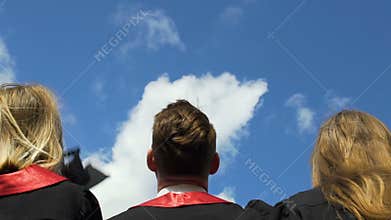 Happy young people celebrating graduation, throwing academic hats up in air