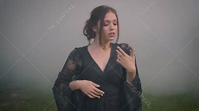 A young, mysterious witch in a black dress conjures in a fog.