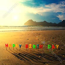 Happy birthday colorful candles on beach sunrise.