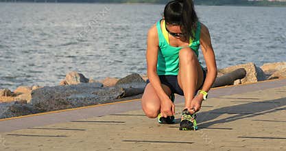 Healthy lifestyle fitness woman runner tying shoelace before running on sunny seaside