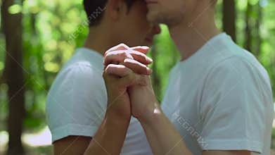 Male lovers joining hands, crossing fingers, outdoor date in park, affection