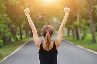 Successful woman raising arms after cross track running on summer sunset. Fitness female athlete with arms up celebrating success