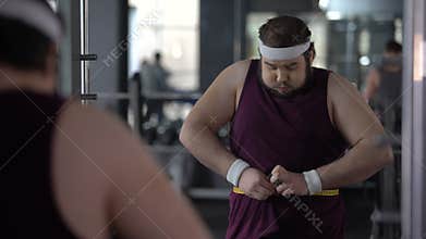 Funny obese man holding his stomach measuring waist with tape, looking satisfied