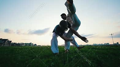 Two athletic men fighting on the grass, one of them knocked the other, summer, sunset