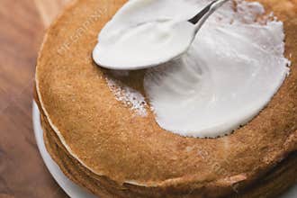 Adiing sour cream to stack of fresh hot crepes or blinis on wood table