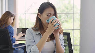 Cheerful asian young businesswoman sitting in office drinking coffee.