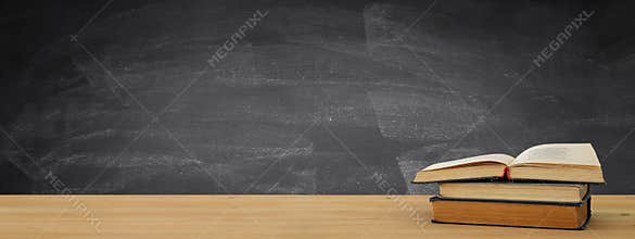 back to school banner. stack of books over wooden desk in front of blackboard.