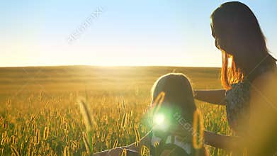 Young mother sitting in field with little blonde daughter and pointing at sunset, happy woman with girl outdoors