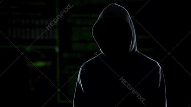 Unknown hooded male hacker looking into camera, global cybercrime problem