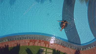 Flycam shows hotel pool with lady sitting on buoy