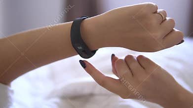 Beautiful woman checking data on her fitness tracker band after waking up in the bed early morning. He is watching