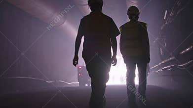 Silhouette of many construction workers walking out from a large tunnel