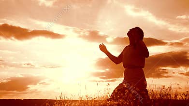 Girl folded her hands in prayer silhouette at sunset. woman praying on her knees. slow motion video. concept