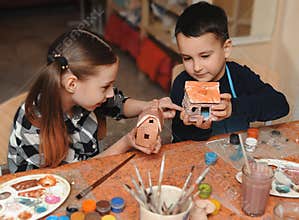 A girl and a boy show each other gouache-painted clay houses