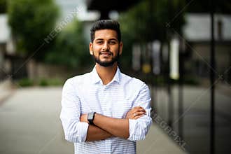 Handsome smiling indian young man with folded arms. Portrait of laughing joyful cheerful men with crossed hands in a city