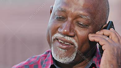 Smiling older black man talking on cellphone closeup, happy grandfather chatting with relatives or grandchildren
