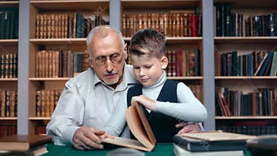 Smiling schooler boy bringing ancient retro book learning history science grandfather at library